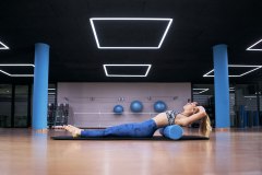 Attractive young woman practicing yoga in a gym, working out in black sportswear, doing some pilates roller exercises.